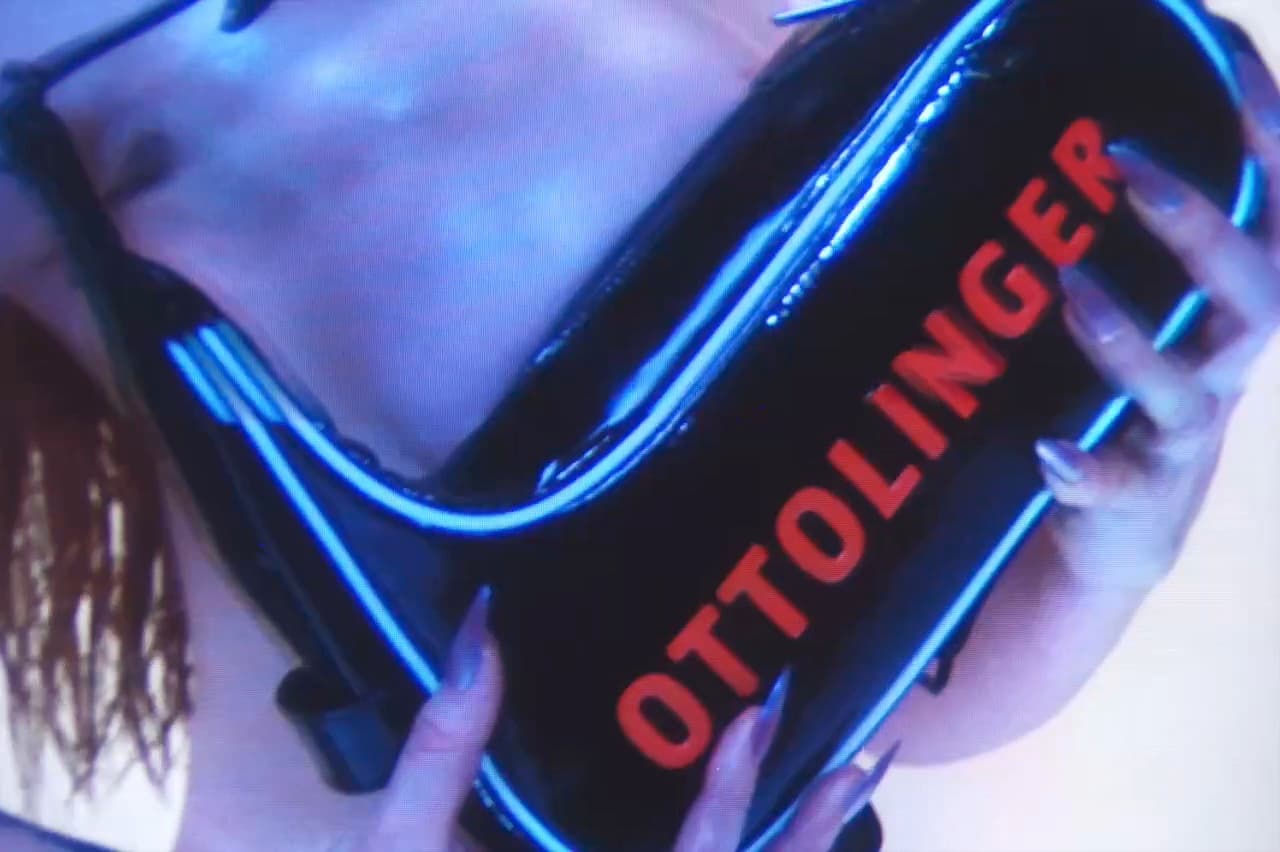 Ottolinger x Puma still, the Ottolinger wordmark across a glossy black garment under blue light.